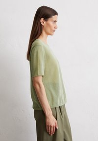 Light green short-sleeved top in a soft, textured knit fabric, with a round neckline and a relaxed fit, paired with loose green pants.