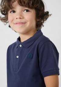 Marineblauwe polo met een gestructureerde stof, twee witte knopen en een ronde rubberen logopatch op de borst. Korte mouwen en een klassieke kraag.