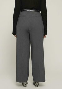 Szare spodnie o szerokich nogawkach wykonane z fakturowanej tkaniny, z dwoma tylnymi kieszeniami, zestawione z czarnym paskiem o wzorze krokodyla i szpilkami w skórę węża.