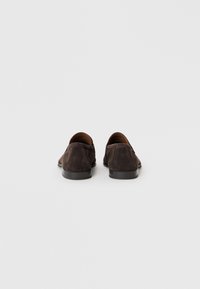 Mocasines de ante marrón oscuro con un acabado suave, punta redondeada, bajo tacón de goma negra y un sutil detalle de costura en el talón y las costuras laterales.