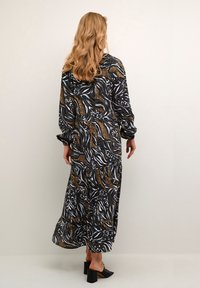 Robe longue noire avec un imprimé animalier tourbillonnant en crème, marron et or. Présente des manches longues et une silhouette décontractée ; se termine aux chevilles.