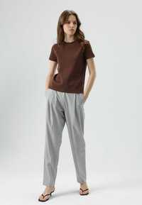 Braunes, enganliegendes T-Shirt mit kurzen Ärmeln, kombiniert mit hellgrauen, plissierten Hosen und schwarzen Sandalen mit Absatz. Einfaches, klares Design mit lockerem Sitz.