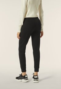 Pantaloni sportivi neri con gamba affusolata, caratterizzati da una texture di tessuto liscia e polsini a coste. Abbinati a scarpe da ginnastica nere e bianche.