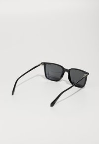 Černé obdélníkové sluneční brýle s tmavými skly. Vyrobené z plastu s elegantními nohami a kovovými akcenty na panty. Hladký povrch, minimalistický design.
