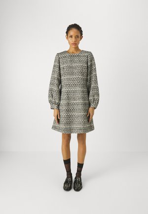 Abito dritto in bianco e nero con texture, caratterizzato da maniche a sbuffo lunghe e una vestibilità ampia, con scollo rotondo e lunghezza fino al ginocchio. Abbinato a scarpe nere.