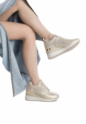 Zapatillas deportivas de plataforma en color beige con diseño perforado, acentos metálicos y una textura suave. Cuentan con una suela de goma blanca.