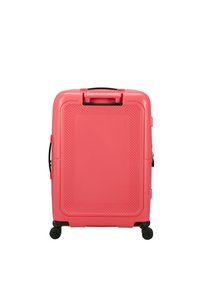 Valigia rigida rosa con design testurizzato, dotata di manico superiore, manico laterale e quattro ruote nere per facilitarne la mobilità.