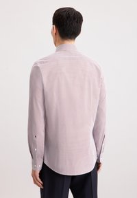 Camicia a maniche lunghe di un rosso chiaro con piccoli pois blu, colletto con bottoni e polsini strutturati. Realizzata in tessuto morbido con una leggera lucentezza.