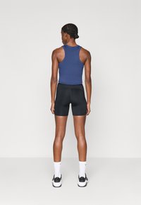 Σκούρο μπλε φανελάκι και μαύρες σορτς με κομψό σχέδιο. Μοντέλο που φοράει λευκές κάλτσες και μαύρα αθλητικά παπούτσια. Λείο υλικό, κοντή εφαρμογή.