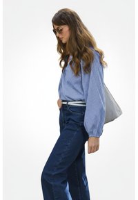 Blauw-wit gestreepte lange mouw shirt, hooggelegen donkerblauwe jeans en een grijze handtas. Heeft een losse pasvorm en elastische manchetten. Zonnebril wordt gedragen.