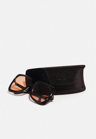 Μαύρα τετράγωνα γυαλιά ηλίου με καφέ φακούς και χρυσές λεπτομέρειες, τοποθετημένα δίπλα σε μία μαύρη βελούδινη θήκη προστασίας με το λογότυπο "TOM FORD".