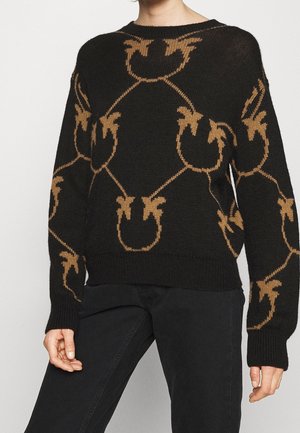 Czarny sweter dziany z brązowym abstrakcyjnym kwiatowym wzorem, noszony z czarnymi spodniami, pokazany od szyi do połowy uda.