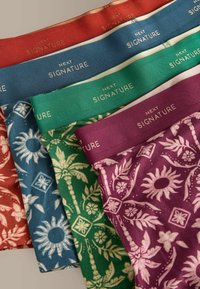 Quatre paires de sous-vêtements à motifs en rouge, bleu, vert et violet, chacune avec une ceinture élastique assortie portant la mention « NEXT SIGNATURE ».