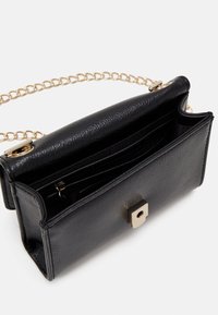 Mustikasta tekstuurista keinonahkainen käsilaukku, jossa on kultaketju ja neliön muotoinen metallisolki. Sisus sisältää useita lokeroita ja vetoketjullisen taskun.