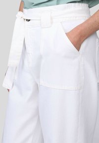 Un pantalon en denim blanc avec une taille haute et une ceinture à nouer, des poches latérales et une coupe décontractée. Texture lisse avec des détails subtils.