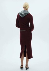 Set in magenta in maglia con un maglione aderente e una gonna di lunghezza media con un'apertura dietro. Il dettaglio grigio con cappuccio sul maglione aggiunge contrasto.