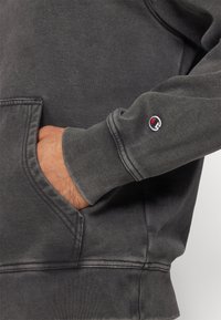 Sweat-shirt gris charbon avec une poche avant, des poignets côtelés et un petit logo brodé sur la manche. Tissu doux et texturé.