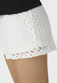 Gros plan sur une personne portant un short en dentelle blanche et un haut noir, mettant en valeur la texture et le motif floral du tissu en dentelle.