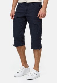 Navy cargo shorts made of cotton, featuring multiple side pockets, adjustable hems, and a smooth texture. Paired with white sneakers.