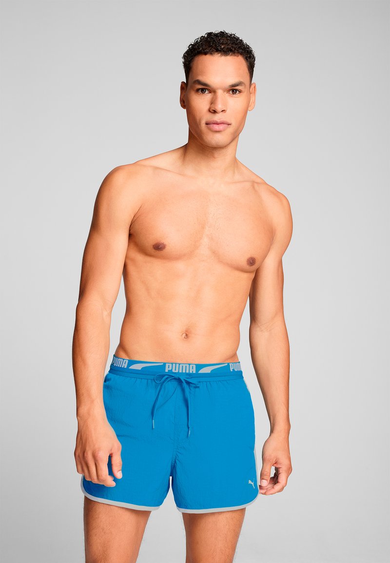 Bañadores azules con cintura elástica, que cuentan con un cordón, detalles grises y un pequeño logo blanco de Puma en la pierna izquierda.