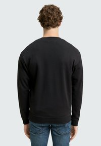 Hanorac negru cu guler rotund, fabrică texturată și mâneci lungi. Asociat cu blugi albaștri, cu tiv și mansete din rib. 