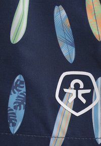 Marinfärgad tyg har färgglada surfbrädemönster i grönt, blått, orange och vitt, med en framträdande vit logotyp längst ner.