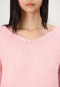 Maglione rosa lavorato a maglia con un ampio scollo a V, caratterizzato da una superficie morbida e testurizzata e una vestibilità ampia, che mette in evidenza i dettagli della cucitura.