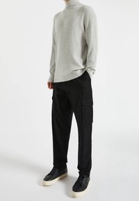 Suéter de tortuga de canalé gris claro combinado con pantalones cargo negros con bolsillos, llevado con zapatillas negras y suelas crema.
