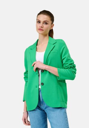 Green, lightweight blazer with a structured design, single button closure, and two front pockets. Worn over a white top and blue jeans.