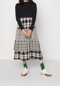 Top negro de manga larga con una falda de capas en patrones a cuadros en blanco y negro. Combinado con zapatillas blancas y calcetines verdes hasta el tobillo.