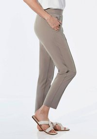 Beige Stretchhosen im Slim-Fit mit seitlichen Taschen und flachem Bund; kombiniert mit hellen Sandalen mit Knotendetails.