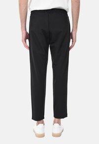 Pantaloni neri aderenti con vita elastica, dotati di tasche laterali, tessuto liscio e polsini attillati, abbinati a sneakers bianche.