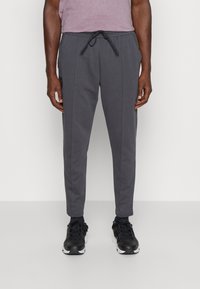 Graue Jogginghosen aus weichem Stoff, mit elastischem Bund und Kordelzug, Seitennähten und schmalem Beindesign. Kombiniert mit schwarzen Sneakers.