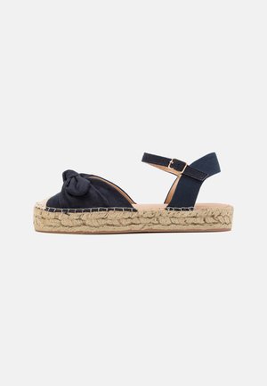 Sandale espadrille bleu marine avec tige en tissu noué, semelle plateforme enveloppée de jute et sangle de cheville maintenue par une boucle en métal.