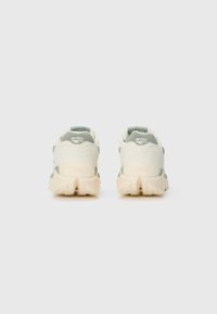 Pair of beige and gray Hi-Tec sneakers viewed from the back on a white surface with Vibram soles visible.