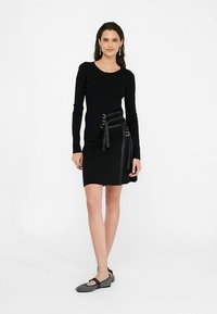 Zwart top met lange mouwen gecombineerd met een korte zwarte rok met lederen accenten en gespen, ontworpen met een aansluitende pasvorm.