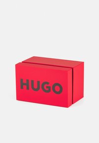Red cardboard box with a matte finish, featuring a prominent black logo that reads "HUGO" on the front, rectangular shape, closed at the top.