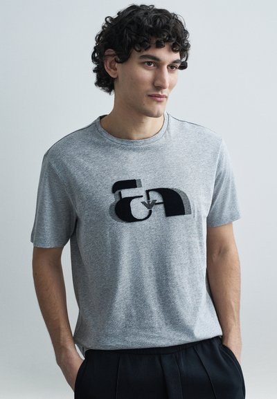 Grå t-shirt med korte ærmer, der har et grafisk motiv i sort. Stoffet virker blødt med en afslappet pasform og rund halsudskæring.