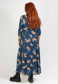 Blaues langärmliges Kleid mit fließendem Design, verziert mit einem Druck verschiedener Tiger. Der Stoff wirkt soft und leicht und wird mit schwarzen Stiefeln kombiniert.