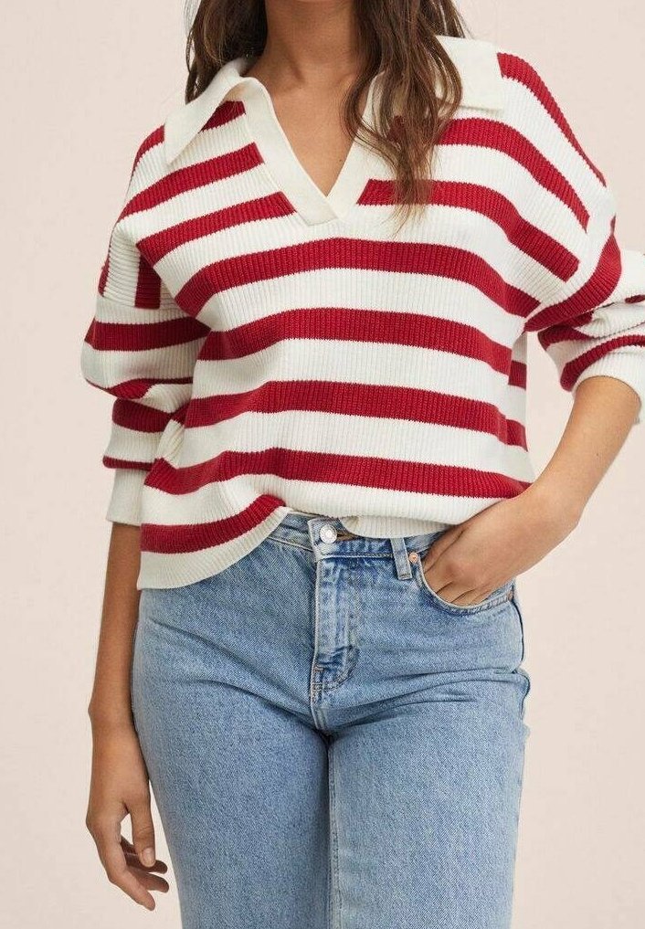 Femme portant un pull en maille blanc et rouge à rayures avec un col en V et un jean taille haute bleu clair, une main dans la poche.