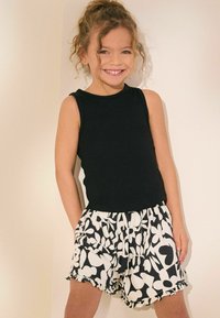Haut noir à côtes sans manches associé à un short blanc avec un motif floral noir audacieux. Le short a une taille élastique et un ourlet froncé.