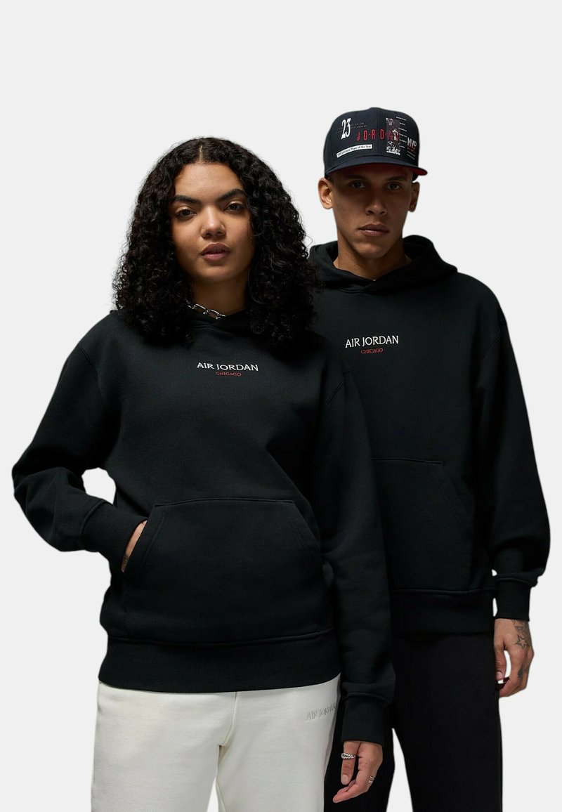 Le felpe nere hanno "AIR JORDAN" ricamato sul petto. Il design presenta una tasca a marsupio e polsini a coste. Il modello a destra indossa un cappellino abbinato.