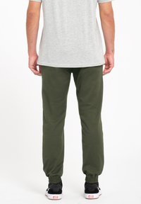 Pantalones de chándal verdes con puños elásticos, hechos de tejido suave. Combinados con una camiseta gris y zapatos negros. Diseño minimalista, sin patrones visibles.