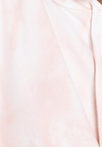 Světle růžová mikina s kapucí, která má měkkou texturu a vybledlý vzor. Obsahuje stahovací šňůrku a žebrované detaily podél okrajů.