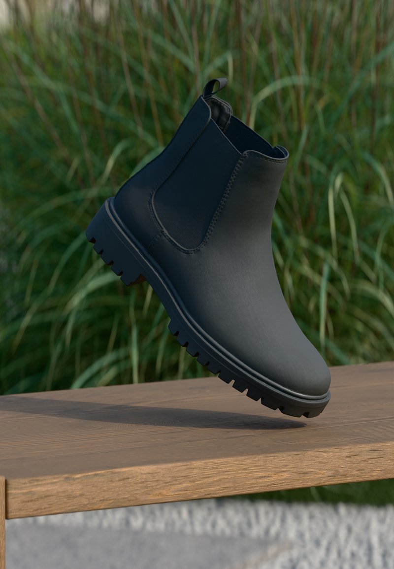 Botín Chelsea negro hecho de material suave, con paneles laterales elásticos, una lengüeta y suela resistente con tacos prominentes.