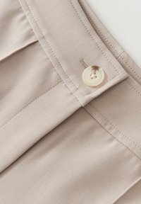 Un tissu beige avec une texture lisse présente un devant plat, une poche lat�érale et un grand bouton couleur crème avec quatre trous.