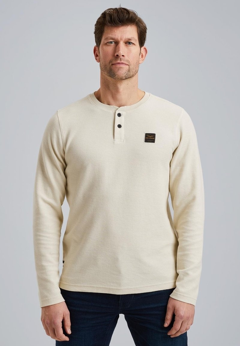 Beige Langarm-Henley-Shirt aus strukturiertem Stoff, mit einem Knopfleiste mit drei Knöpfen und einem kleinen Logo-Patch auf der Brust.