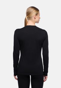 Schwarzes Langarmshirt mit Rundhalsausschnitt und figurbetontem Schnitt. Verfügt über gestickte Nähte und ein kleines grünes Etikett am Saum. Glatte Stofftextur.