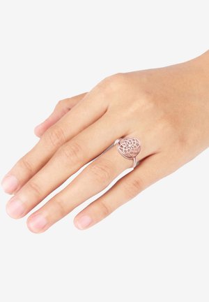 Rose gold metalring med et intrikat, åbent blomsterdesign på en slank ringe, vist på en hånd med naturlige negle.
