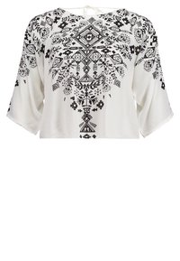 Haut court blanc avec broderies noires géométriques et florales. Comprend des manches larges et un détail noué au niveau du col. Texture de tissu douce.